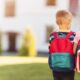 Little boy and girl with school backpacks holding hands and walking away from home