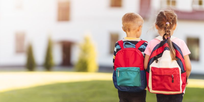 Little boy and girl with school backpacks holding hands and walking away from home